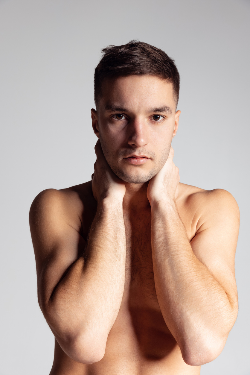 Junger, dunkelhaariger Mann bedeckt seinen Oberk&ouml;rper besch&auml;mt mit den Unterarmen.