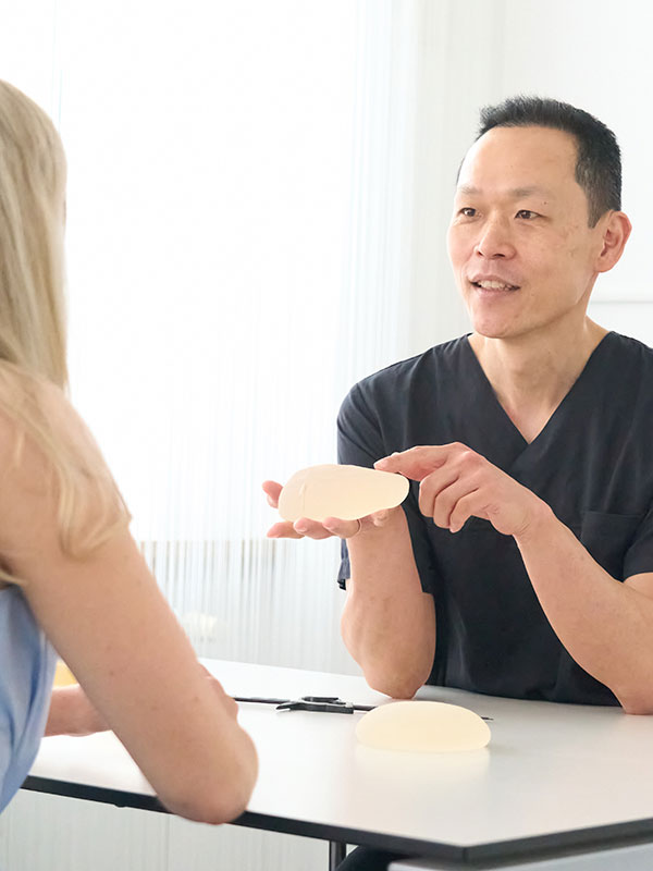 Der Arzt zeigt einer blonden Patientin ein Brustimplantat.