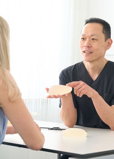 Der Arzt zeigt einer blonden Patientin ein Brustimplantat.