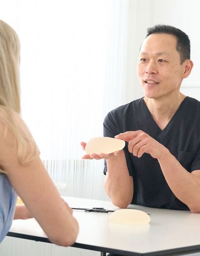 Der Arzt zeigt einer blonden Patientin ein Brustimplantat.