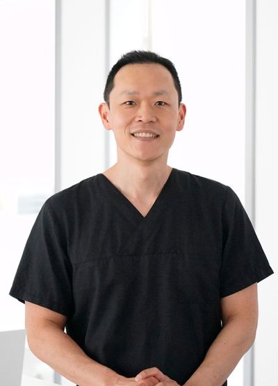 Dr. Yun mit dunklem Oberteil schaut lächelnd in nach vorne